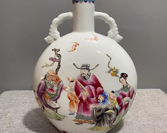 Op de afbeelding: Witte keramische vaas met een ronde body, twee handvatten en een smalle hals. De vaas heeft een kleurrijke illustratie van figuren in traditionele kleding. De rand heeft een decoratief blauw en groen patroon.