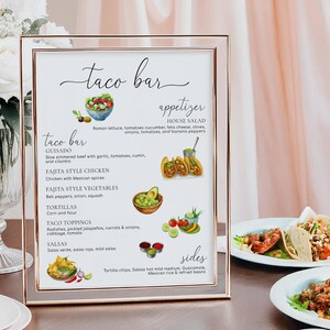 May include: A rectangular sign in a thin rose gold frame featuring the text Taco Bar, Appetizer, and Sides. The menu lists food items including Guisado, Fajita Style Chicken, Fajita Style Vegetables, Tortillas, Taco Toppings, and Salsas with watercolor illustrations of various ingredients like avocados, tomatoes, and peppers.