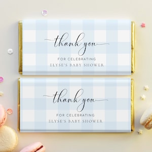 Könnte beinhalten: Zwei blaue und weiße Gingham-Schokoladenriegel-Verpackungen mit goldenen Folienrändern. Die Verpackungen haben den Text "Danke" in einer kursiv geschriebenen Schrift und den Text "für die Feier von Elises Babyparty".