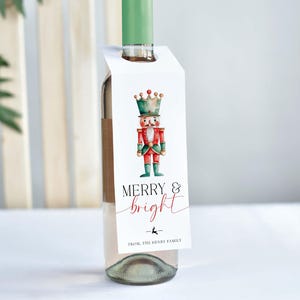 May include: A wine bottle with a white tag featuring a watercolour illustration of a nutcracker soldier in red, green, and gold. The tag reads "MERRY & bright" in a script font, with a small reindeer graphic.