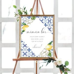 May include: A printable sign with a blue and white tile pattern and lemons and white flowers. The sign says "mimosa bar" and includes instructions for making mimosas: "Pour some bubbly, add some juice, top with fruit, cheers!"