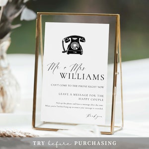 May include: A white rectangular sign in a gold metal frame featuring a black illustration of a rotary telephone and the text: Mr + Mrs WILLIAMS, CAN'T COME TO THE PHONE RIGHT NOW, LEAVE A MESSAGE FOR THE HAPPY COUPLE, and instructions for guests.