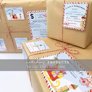 Peut inclure: Plusieurs cadeaux emball&eacute;s avec des &eacute;tiquettes festives et de la ficelle. Les &eacute;tiquettes pr&eacute;sentent des illustrations du P&egrave;re No&euml;l, des elfes et un tra&icirc;neau, avec le texte "Santa's Workshop" et "Handle with Care". Les cadeaux sont emball&eacute;s dans du papier brun.