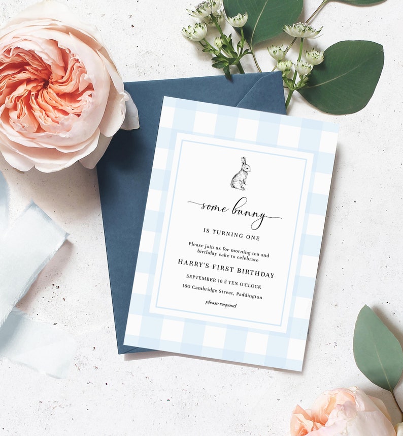 Może przedstawiać: Niebieskie zaproszenie w kratkę vichy z napisem "some bunny is turning one" i małą ilustracją kr&oacute;lika. Zaproszenie jest na pierwsze urodziny Harry'ego i zawiera datę, godzinę i miejsce. Granatowa koperta i r&oacute;żowe kwiaty w tle.