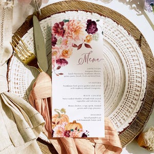 May include: A menu card with floral accents, featuring a fall-themed design. The card displays a menu with appetizers, starters, main courses, and dessert options. The menu is set on a decorative plate with a gold fork and knife.