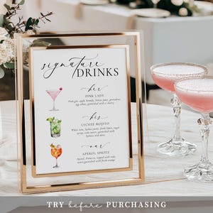May include: A gold-framed sign with the words "Signature Drinks" and drink descriptions, including a Pink Lady, Lychee Mojito, and Aperol Spritz. Two pink cocktails in elegant glasses are in the background. The sign includes the text "TRY before PURCHASING".