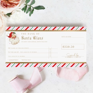 May include: A Christmas-themed cheque from "The Bank of Santa Claus" with a vintage Santa illustration. The cheque has red, green, and pink candy cane stripes, gold accents, and space for the recipient's name and amount. The amount is £198.75.