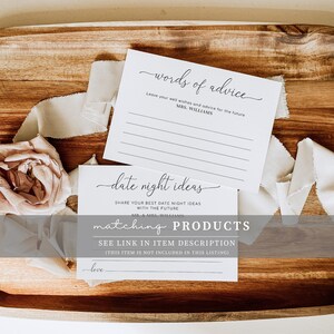 Pu&ograve; includere: Due carte bianche con testo nero. La carta superiore dice "words of advice" e ha delle righe per scrivere. La carta inferiore dice "date night ideas" e ha una riga per scrivere. Le carte sono su una superficie di legno con un fiore rosa e un nastro bianco.