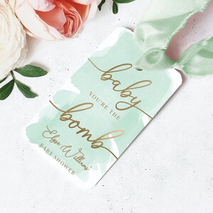 Etiqueta de regalo con texto "Baby You're The Bomb", etiqueta de regalo con texto "Baby Shower" y "Agradecimiento" en papel dorado con acuarela verde.