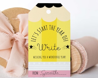 Op de afbeelding: Een gele en zwarte potloodvormige cadeau-tag met de tekst "Let's start the year off Write" en "Wishing you a wonderful year!" De tag heeft een roze gedeelte onderaan met de tekst "From: Samantha".