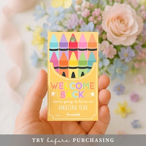 May include: A yellow card with a crayon box design, featuring the text "WELCOME BACK" and "we're going to have an AMAZING YEAR". The card is held in a hand, with a floral background.