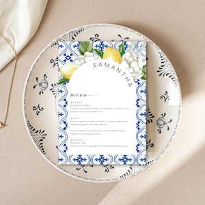 Puede incluir: Una tarjeta de menú de boda con un fondo estampado en azul y blanco. La tarjeta presenta una ilustración de acuarela de limones y flores blancas. El texto en la tarjeta dice "Samantha" y "Menú". El menú incluye entrantes, platos principales y postres.