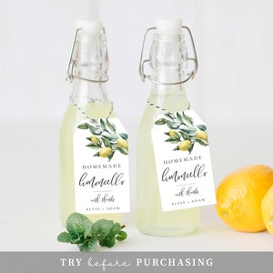May include: Two small glass bottles filled with a yellow liquid, each with a white tag attached. The tags feature a watercolor illustration of lemons and leaves, and the text "HOMEMADE limoncello with thanks ELYSE ADAM".