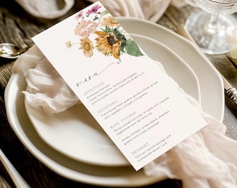 May include: A white menu card with a floral design featuring sunflowers and other flowers. The menu card lists appetizers, starters, main course, and dessert options. The text on the menu card reads: "meru", "APPETIZER", "Antipasto Platters", "Local charcuterie, farmhouse cheeses, quince paste, lavosh, fresh and dried fruit.", "STARTERS", "Farmhouse fresh greens garden salad served with raspberry infused vinaigrette.", "MAIN COURSE", "Twice-cooked shoulder of lamb with roasted vegetables and red wine jus.", "Honey chicken, crispy speck, steamed greens and crispy potatoes.", "DESSERT", "Tahition Vanilla sponge with homemade lemon curd."