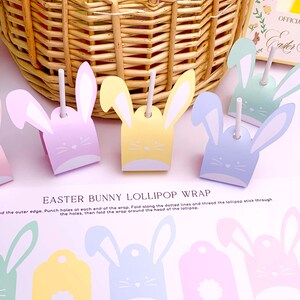 Könnte beinhalten: Osterhasen-Lutscherverpackungen in Pastellfarben: Rosa, Gelb, Blau und Grün. Jede Verpackung hat Hasenohren und ein Gesicht, mit einem Lutscherstiel. Der Text "EASTER BUNNY LOLLIPOP WRAP" ist sichtbar.