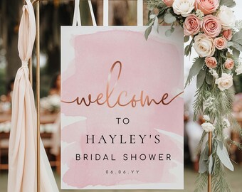 Op de afbeelding: Een roze aquarel bruiloft douche welkomstbord met gouden letters die "Welkom bij Hayley's Bridal Shower 06.06.YY" zeggen.
