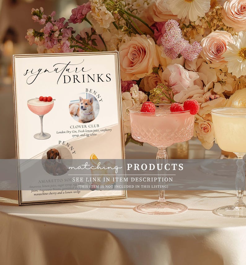 May include: A framed sign with "Signature Drinks" text, featuring illustrations of cocktails and pet portraits. A pink cocktail with raspberries sits in a crystal glass. Floral arrangements and a second cocktail glass are in the background.