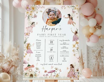 May include: A personalized 'Fairy First Year' sign on an easel, featuring a baby's photo and details. The sign includes the name 'Harper's', weight 22 pounds, height 31 inches, and favorite things. The design incorporates fairy illustrations and floral accents.