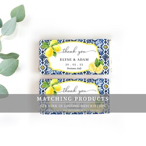 May include: Two blue and white tiled favor boxes with a lemon design. The top box says "thank you" and "Elyse & Adam" with the date "20.02.22" and "Positano, Italy". The bottom box says "thank you" and "MATCHING PRODUCTS" with the date "20.02.22" and "Positano, Italy". The text "SEE LINK IN LISTING DESCRIPTION (THIS ITEM IS NOT INCLUDED IN THIS LISTING)" is also on the bottom box.