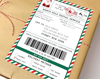 Może przedstawiać: Prostokątna etykieta wysyłkowa North Pole Postal Service z czerwono-zieloną ukośnie paskowaną ramką. Etykieta zawiera grafikę Świętego Mikołaja, czerwony stempel pocztowy, tekst zaadresowany do Mili Grace, kod kreskowy oraz opcje dostawy.