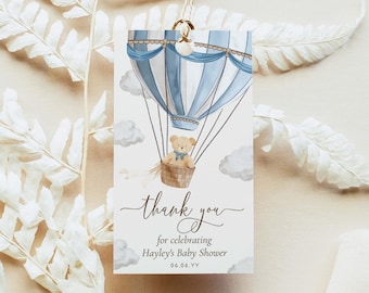 May include: A blue and white hot air balloon with a teddy bear in the basket. The balloon is surrounded by clouds. The text "thank you" is written in cursive below the balloon. The text "for celebrating Hayley's Baby Shower 06.06.YY" is written below the cursive text.