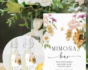 May include: A sign with a floral design and the text "Mimosa Bar" with instructions to "Pour some bubbly, add some juice, top with fruit, sip & enjoy". Two small glass bottles with tags that say "Orange Juice" and "Lychee Juice" are in the foreground.