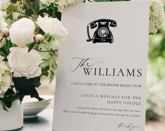 May include: A white sign with black text and a black and white illustration of a rotary phone. The text reads "The Williams Can't Come to the Phone Right Now Leave a Message for the Happy Couple Pick up the phone and leave a message after the tone. When you're finished hang up to ensure your message is recorded. Thank you."