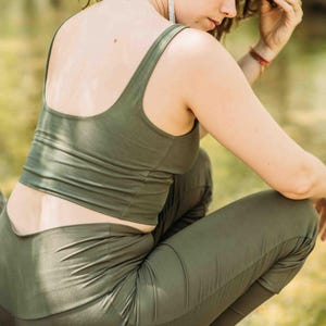 Pu&ograve; includere: Completo sportivo verde oliva. Il set include un top corto con scollo tondo e leggings abbinati. Il tessuto sembra morbido e aderente. La modella &egrave; accovacciata all'aperto, suggerendo che l'abbigliamento &egrave; adatto per yoga o altre attivit&agrave;.