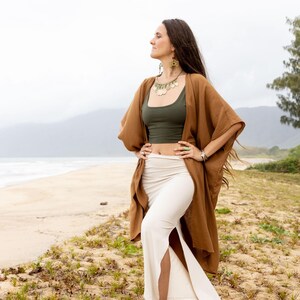 K&ouml;nnte beinhalten: Ein olivgr&uuml;nes bauchfreies Tanktop kombiniert mit einem cremefarbenen, hoch taillierten Maxirock mit Seitenschlitz, getragen unter einer offenen, braunen Kimono-Strickjacke mit weiten &Auml;rmeln. Das Outfit wird durch eine goldfarbene Kette erg&auml;nzt.