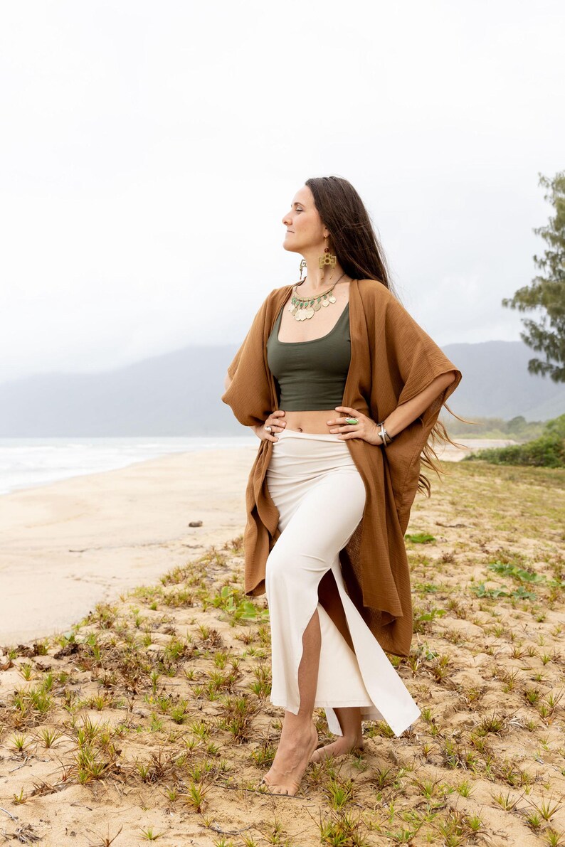 K&ouml;nnte beinhalten: Ein olivgr&uuml;nes bauchfreies Tanktop kombiniert mit einem cremefarbenen, hoch taillierten Maxirock mit Seitenschlitz, getragen unter einer offenen, braunen Kimono-Strickjacke mit weiten &Auml;rmeln. Das Outfit wird durch eine goldfarbene Kette erg&auml;nzt.