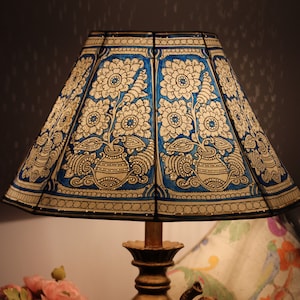 May include: A decorative table lamp with a blue and white floral patterned lampshade. The lamp base features a gold-colored elephant figurine. A vase of pink flowers is visible in the foreground.