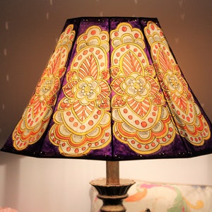 May include: A purple lampshade with a hand-painted design of orange and yellow flowers. The lampshade is made of fabric and has a geometric shape.