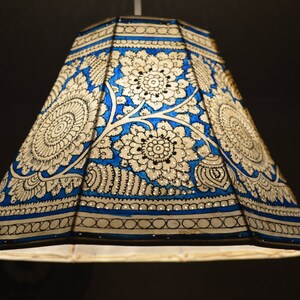 Puede incluir: Pantalla de lámpara decorativa con un diseño floral azul y blanco. La pantalla tiene forma cónica y está adornada con intrincados patrones. El diseño presenta grandes flores estilizadas y bordes detallados, creando un efecto visual llamativo.