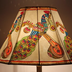 May include: A decorative lampshade featuring a hand-painted design of colorful peacocks and musical instruments. The artwork includes vibrant hues of orange, blue, green, and yellow. The lampshade is a unique home decor item.