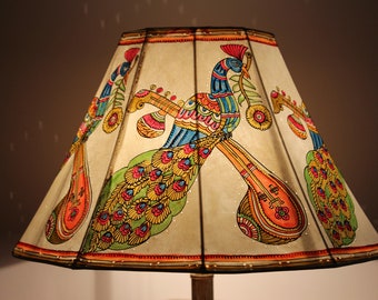 May include: A decorative lampshade featuring a hand-painted design of colorful peacocks and musical instruments. The artwork includes vibrant hues of orange, blue, green, and yellow. The lampshade is a unique home decor item.