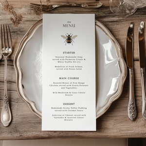 Puede incluir: Un menú blanco con una ilustración de abeja negra y el texto "the MENU". El menú enumera un entrante, un plato principal y un postre con descripciones de cada plato.