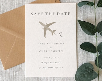 May include: A white rectangular Save the Date card featuring a gray airplane graphic with a dotted flight path. The text reads: SAVE THE DATE, HANNAH HUDSON & CHARLIE GREEN, 29th May 2023, St Regis Bali Resort, formal invite to follow.