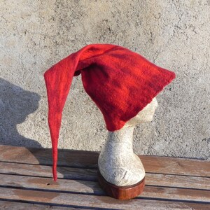 May include: A red felt hat with a long pointed tip. The hat is on a mannequin head and is displayed against a textured wall.