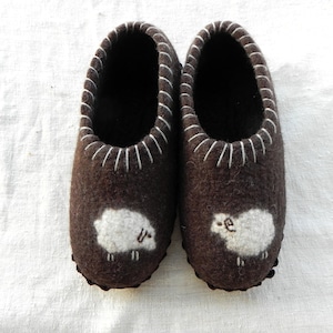May include: A pair of brown felt slippers with white sheep embroidered on the toes.
