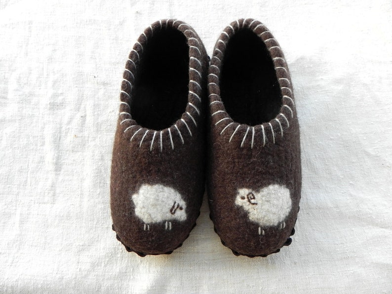 May include: A pair of brown felt slippers with white sheep embroidered on the toes.
