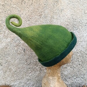 May include: A felted hat in shades of green featuring a tall, pointed crown that curls at the tip. The hat has a dark green folded brim and a gradient color transition from a lighter lime green at the top to a deeper forest green at the base.