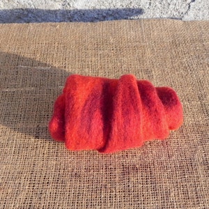 May include: A red and orange wool scarf rolled up on a burlap surface.