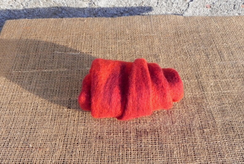 May include: A red and orange wool scarf rolled up on a burlap surface.