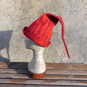 May include: A red felt hat with a long pointed tip. The hat is on a white mannequin head.