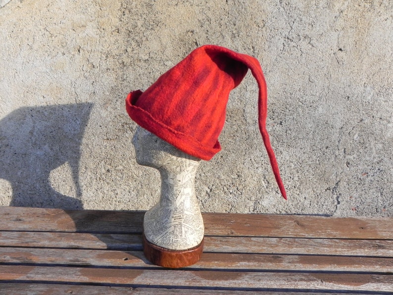 May include: A red felt hat with a long pointed tip. The hat is on a white mannequin head.
