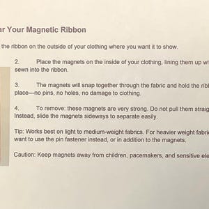 May include: Instructions on how to wear a magnetic ribbon. The text explains how to position the ribbon, align the magnets, and remove the ribbon. A small package with a ribbon and magnets is shown.