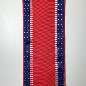 May include: A red ribbon with blue borders featuring white stars. The ribbon has a vertical design, with a solid red center and blue and white star patterned edges. The ribbon is likely for crafting or decoration.