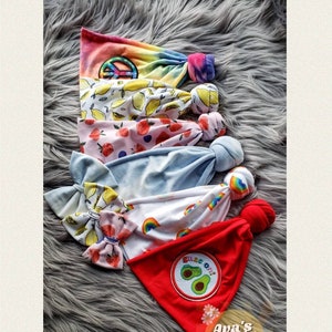May include: A collection of colorful headbands with various patterns, including tie-dye, lemons, strawberries, and rainbows. One red headband features an avocado patch with the text "Peace Out". The headbands are knotted at the top.