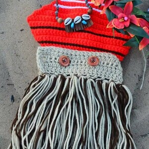 May include: A handmade crochet costume in the style of a Polynesian princess. The top is red with black stripes, and the skirt is made of brown and white yarn. The costume includes a necklace with shells and wooden beads, and is decorated with red flowers.