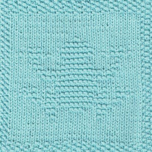 May include: Close-up of a knitted square in a light turquoise colour. The square features a textured tree design in the centre, surrounded by a textured border. The knitting pattern is visible throughout the piece.